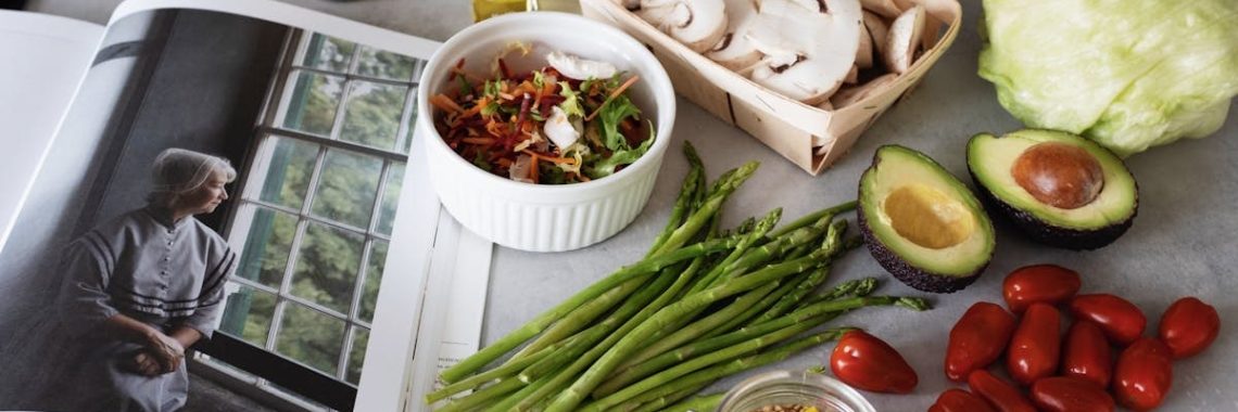 A selection of fresh vegetables and a cookbook in a kitchen setting, promoting healthy cooking.