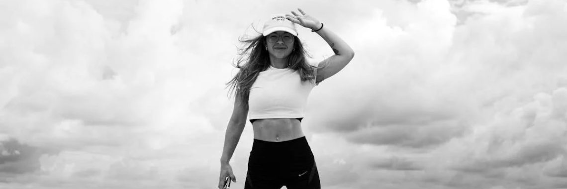 Woman in sportswear stands confidently by the sea against a cloudy sky.